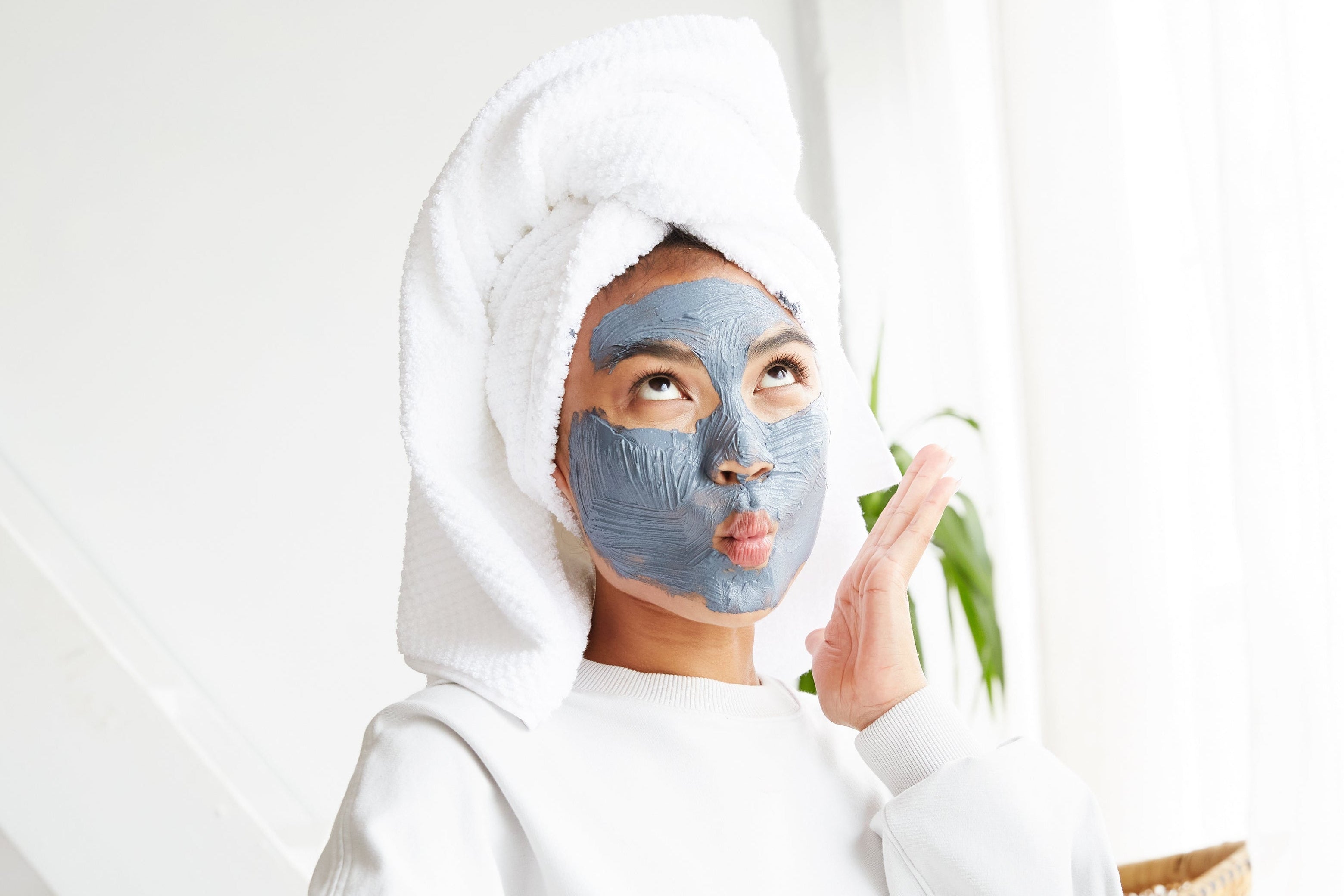 Woman applying facial mask with towel on head in a bright room